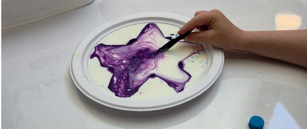 Purple dye spreading into swirls across a plate of milk